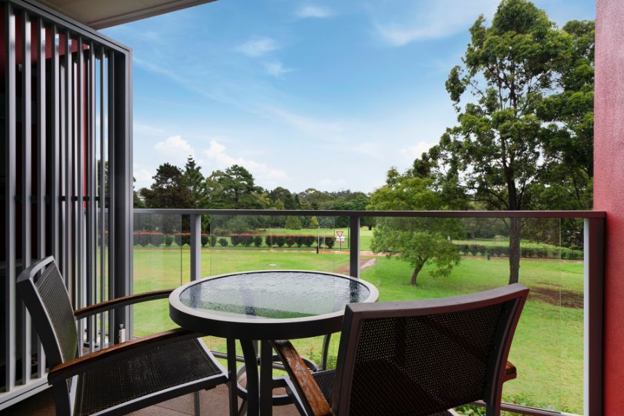 Balcony with glass table and chairs overlooking a green lawn and trees