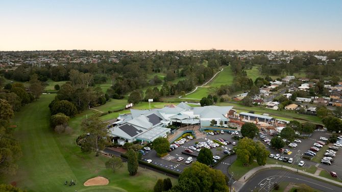Aerial view of a City Golf Club building with parking lots, trees, and a golf course at sunset