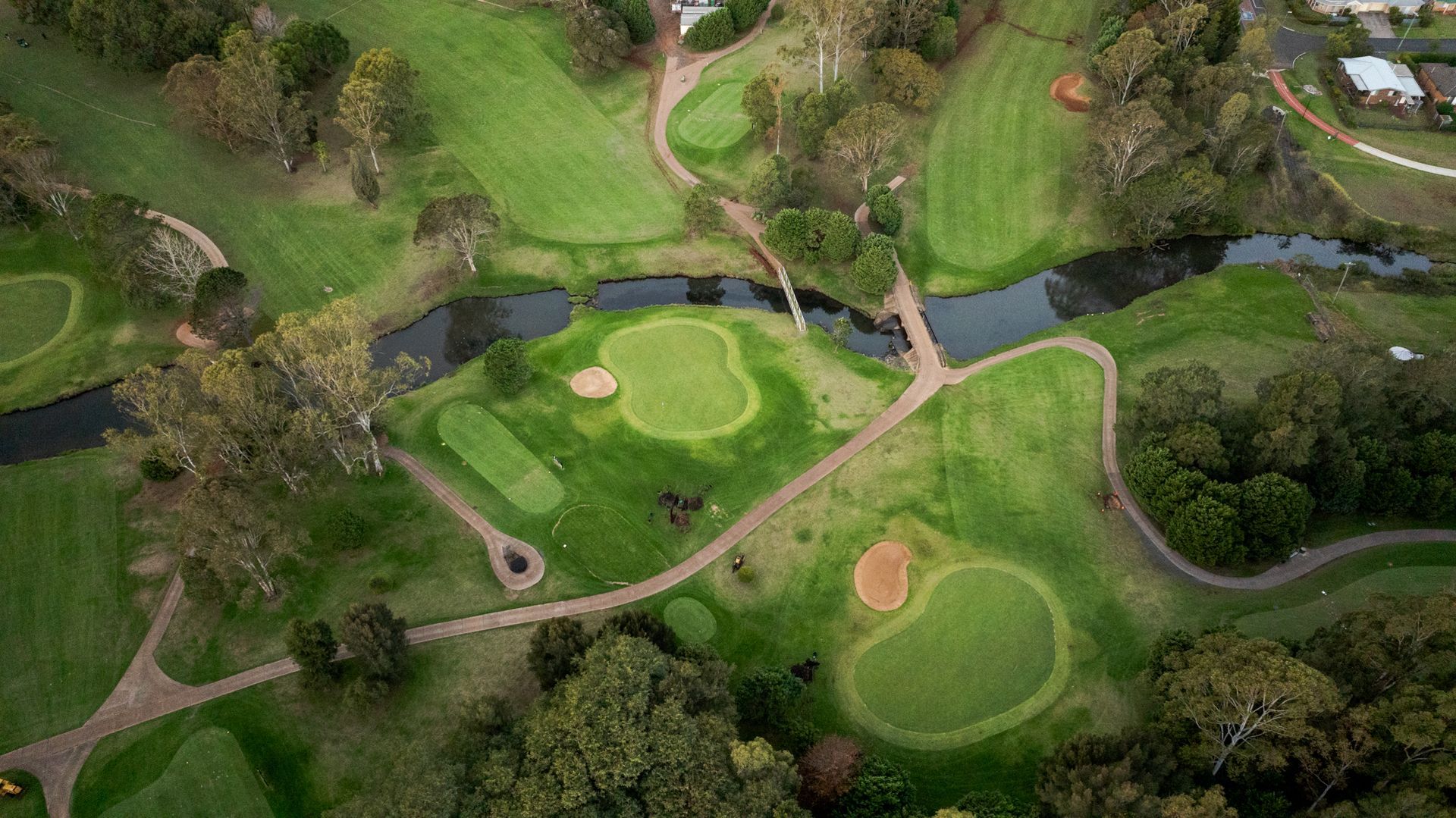 Aerial view of a golf course with green fairways, sand bunkers, trees, and winding cart paths.