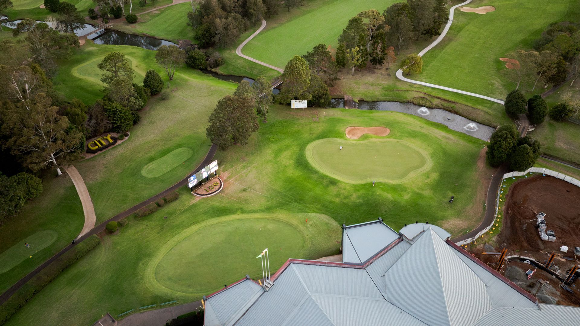 Aerial view of a golf green with a flag, bunker, and surrounding trees and fairways