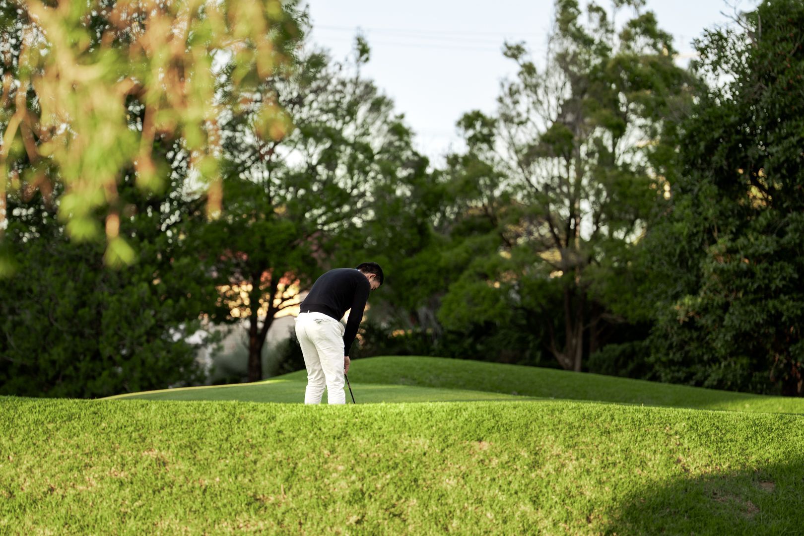 Golfer in dark shirt and white pants putting on a green golf course