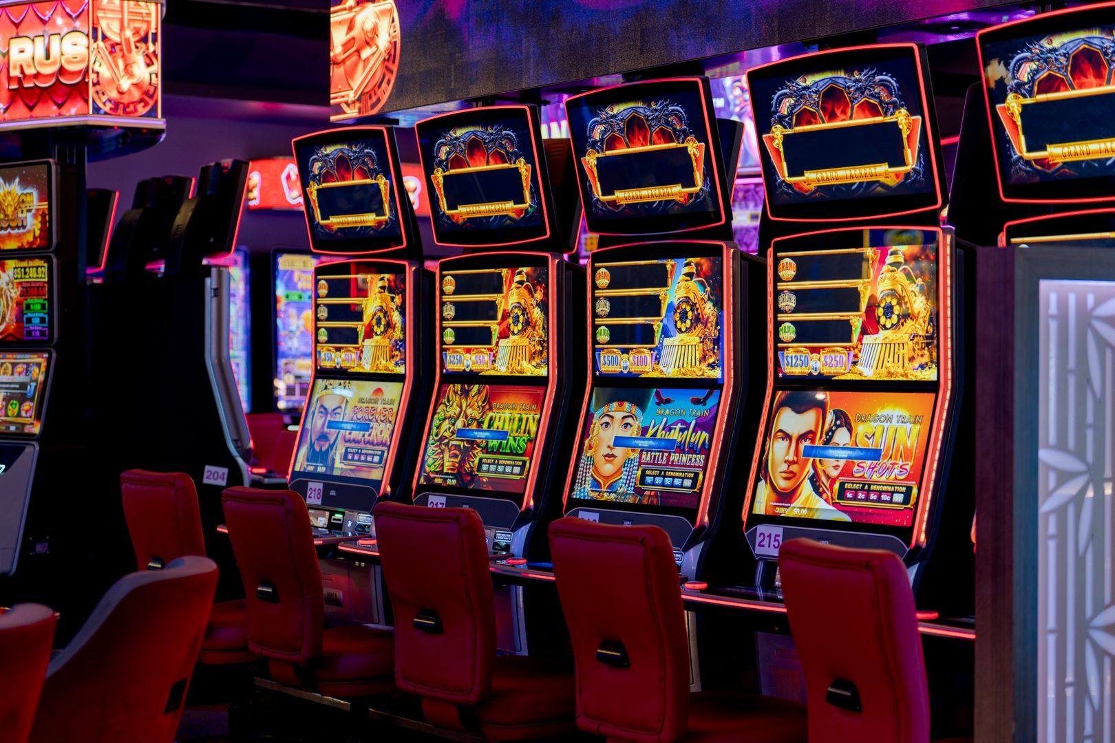 Rows of colourful slot machines with red chairs in a bright casino arcade
