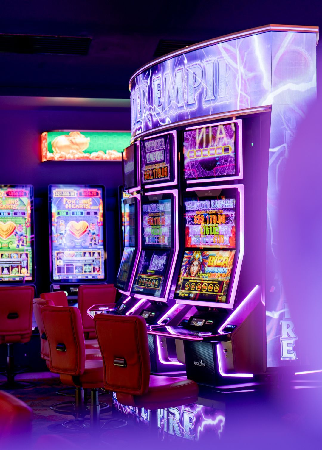 Neon-lit casino slot machines in a purple arcade with red chairs and glossy floor reflections