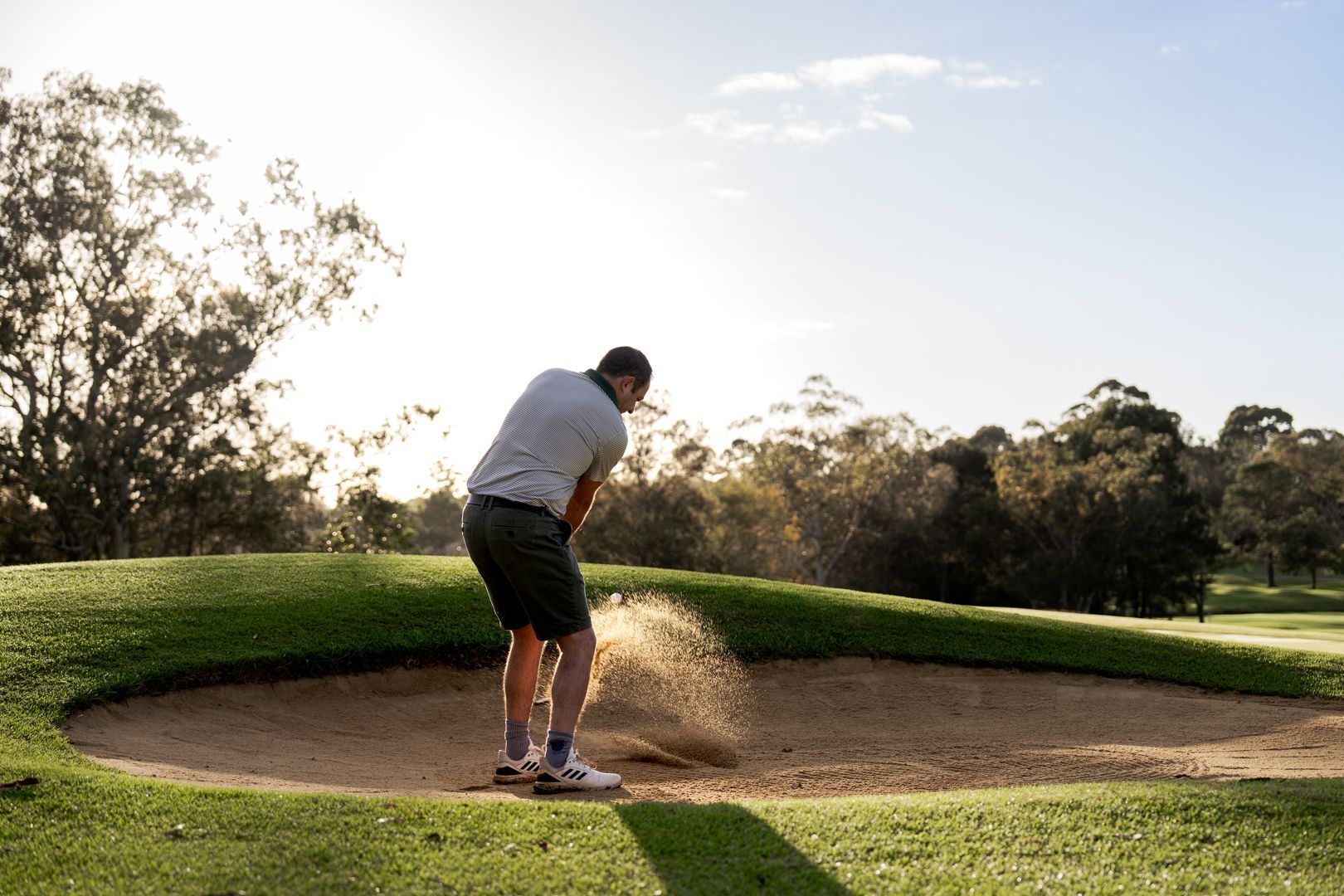 Golfer hitting a shot from a sand bunker on a sunny course