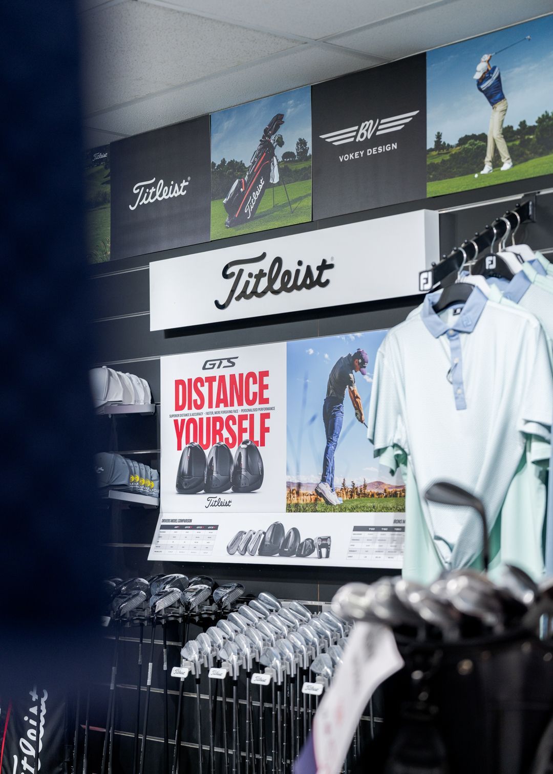 Golf apparel display with Titleist sign, “Distance Yourself” poster, and hanging shirts in a retail store