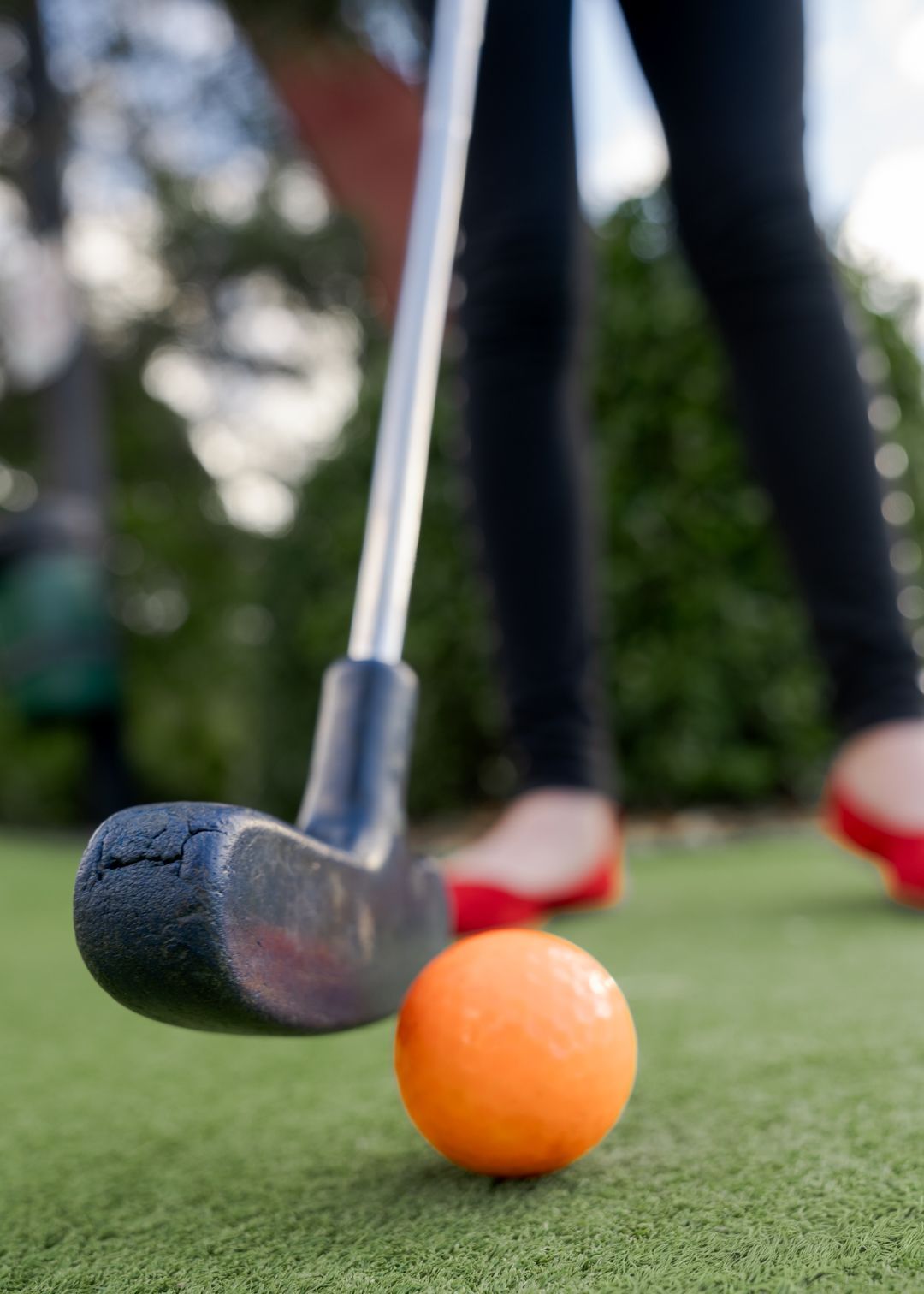 Golfer putting an orange ball on green turf with a putter