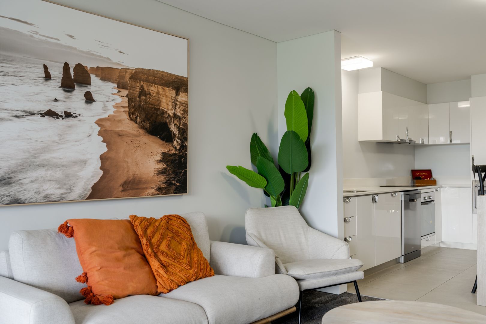 Bright modern motel room with white sofa, orange pillows, large wall art, and a tall green plant.