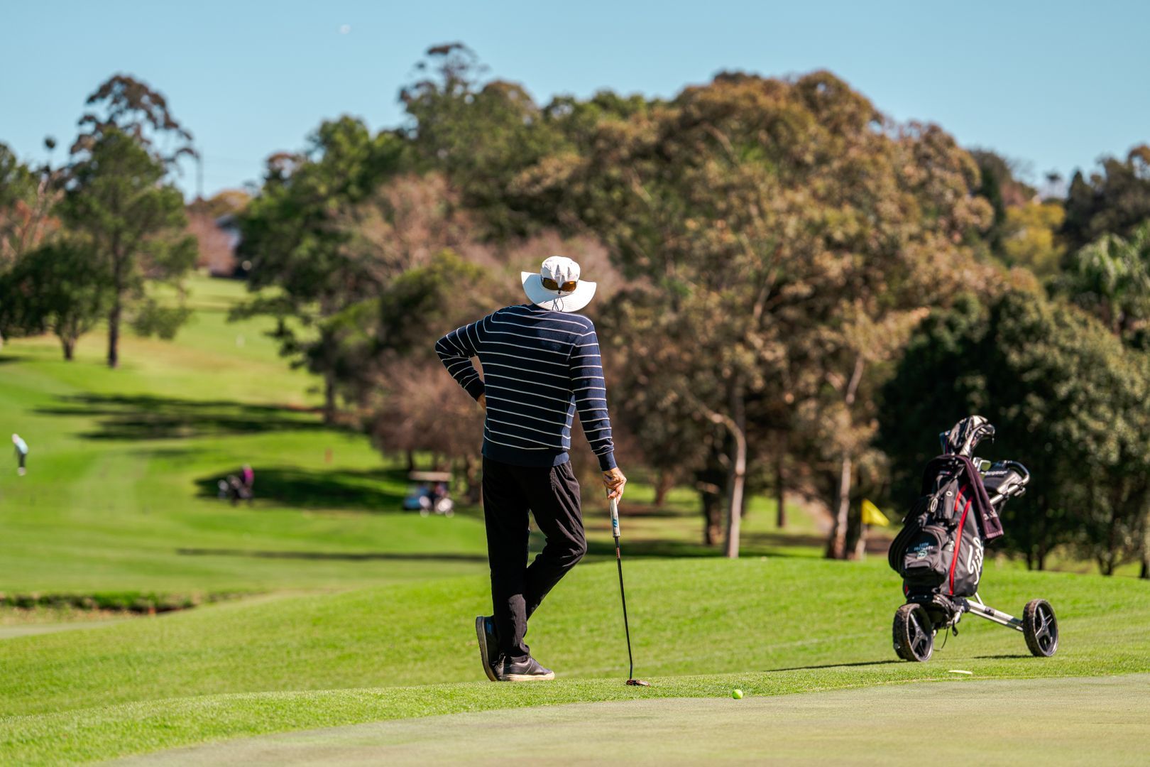 Golfer walking on a green fairway beside a golf cart on a sunny course
