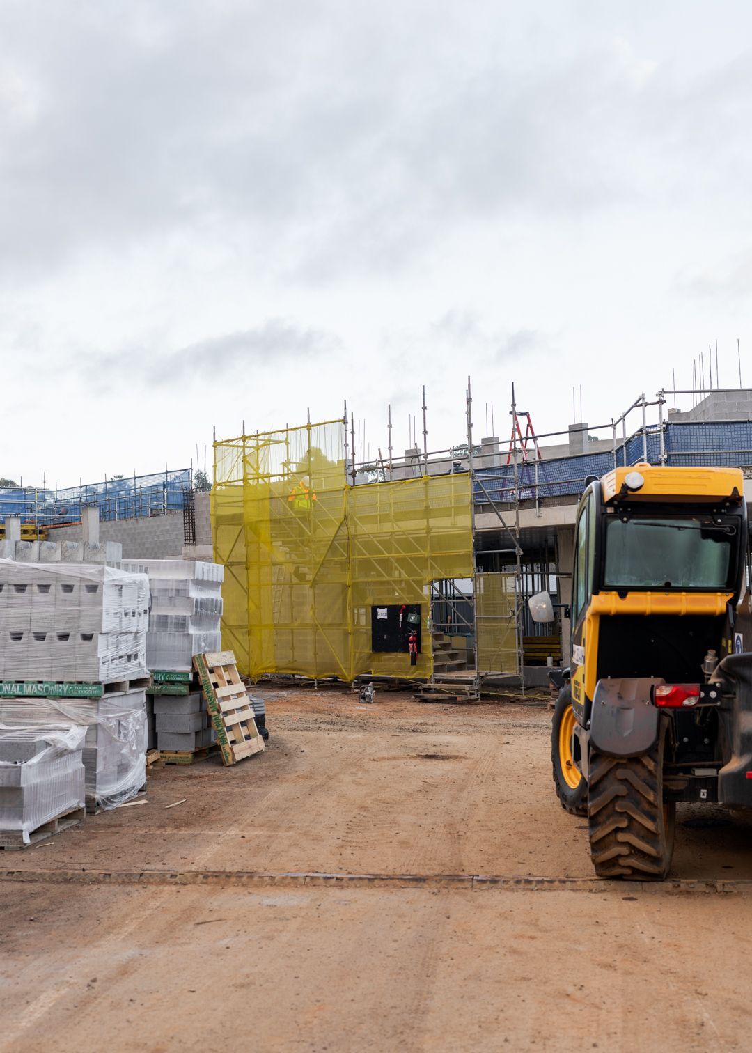 Construction site with yellow scaffolding, stacked materials, and a front loader on a dirt path