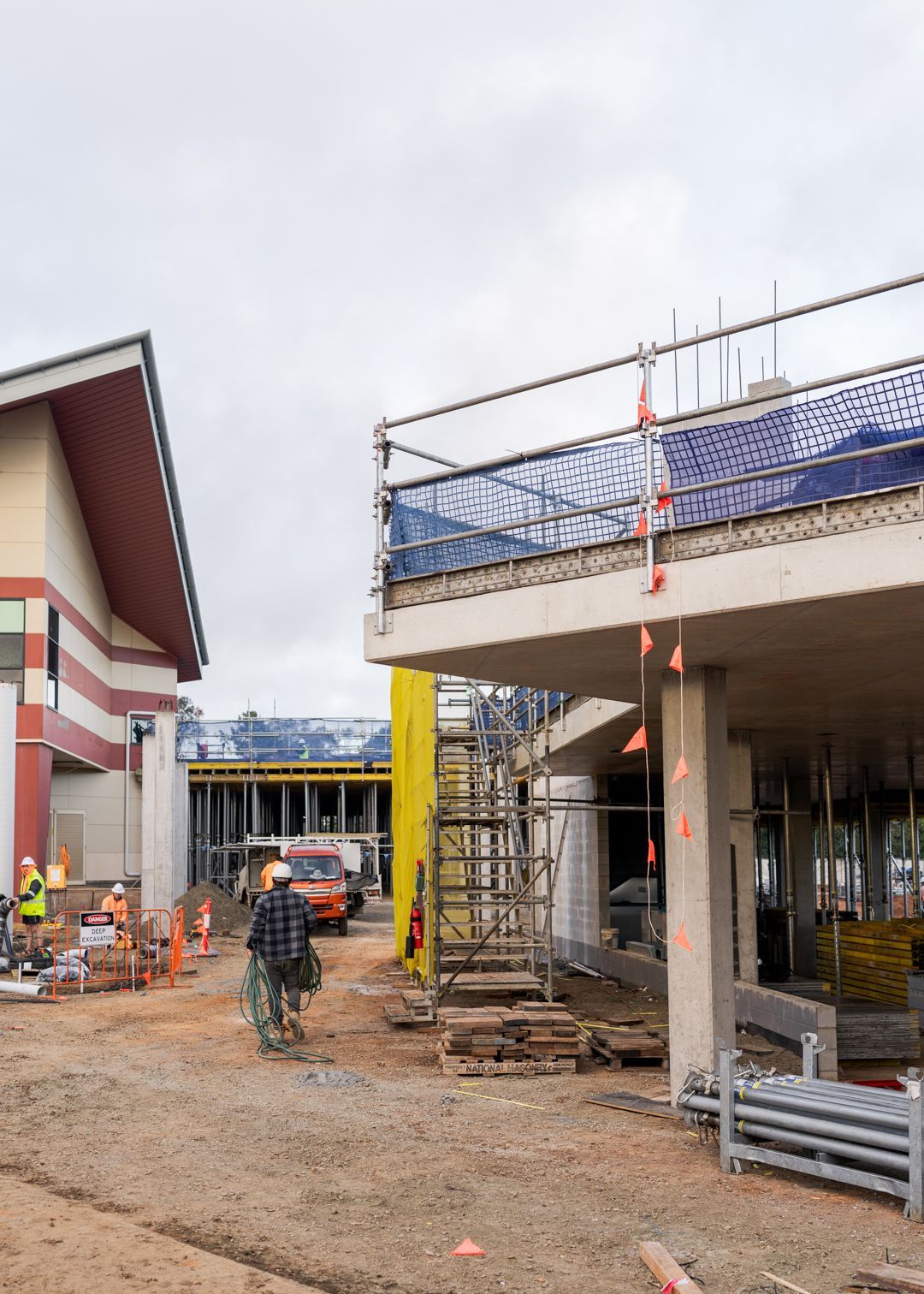Construction site with workers, a cyclist, and partially built concrete structures under cloudy skies