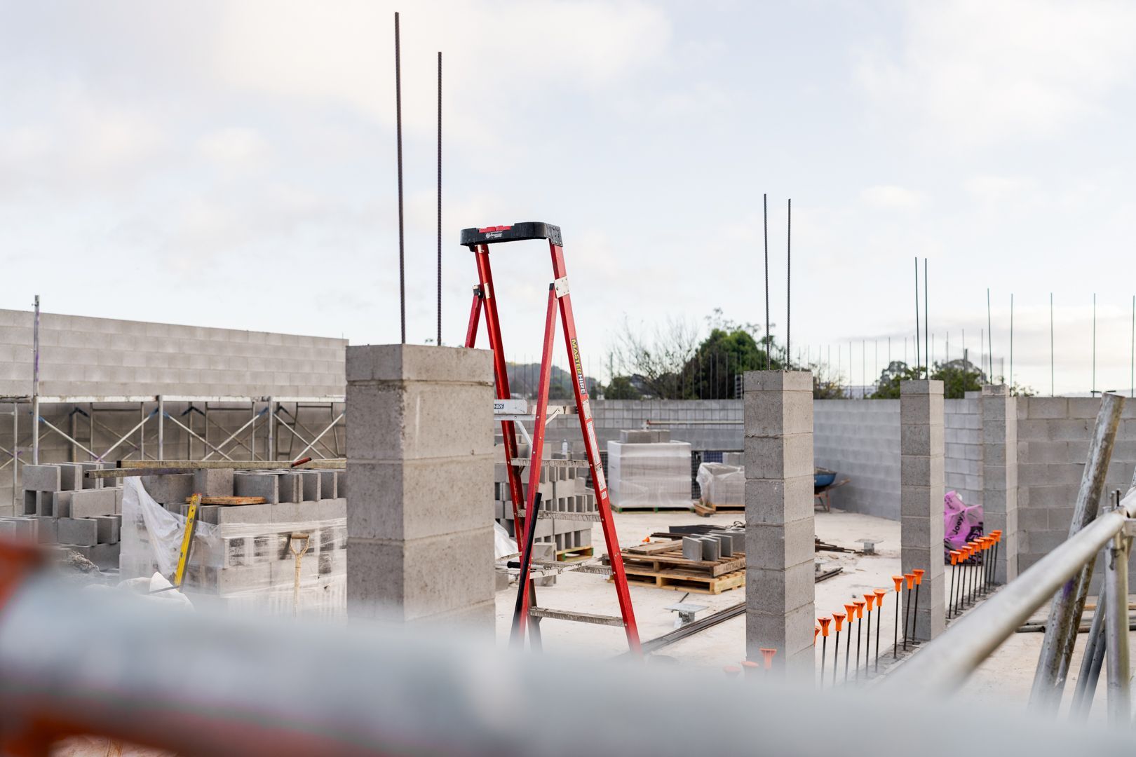 Construction site with red ladder, concrete walls, and workers in the background