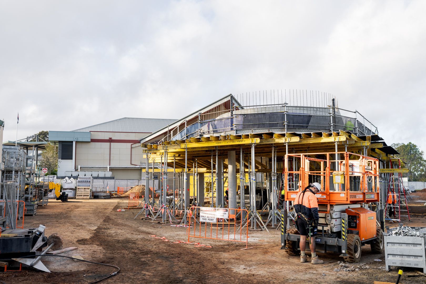 Construction site with a partially built yellow structure, scaffolding, and orange machinery on muddy ground