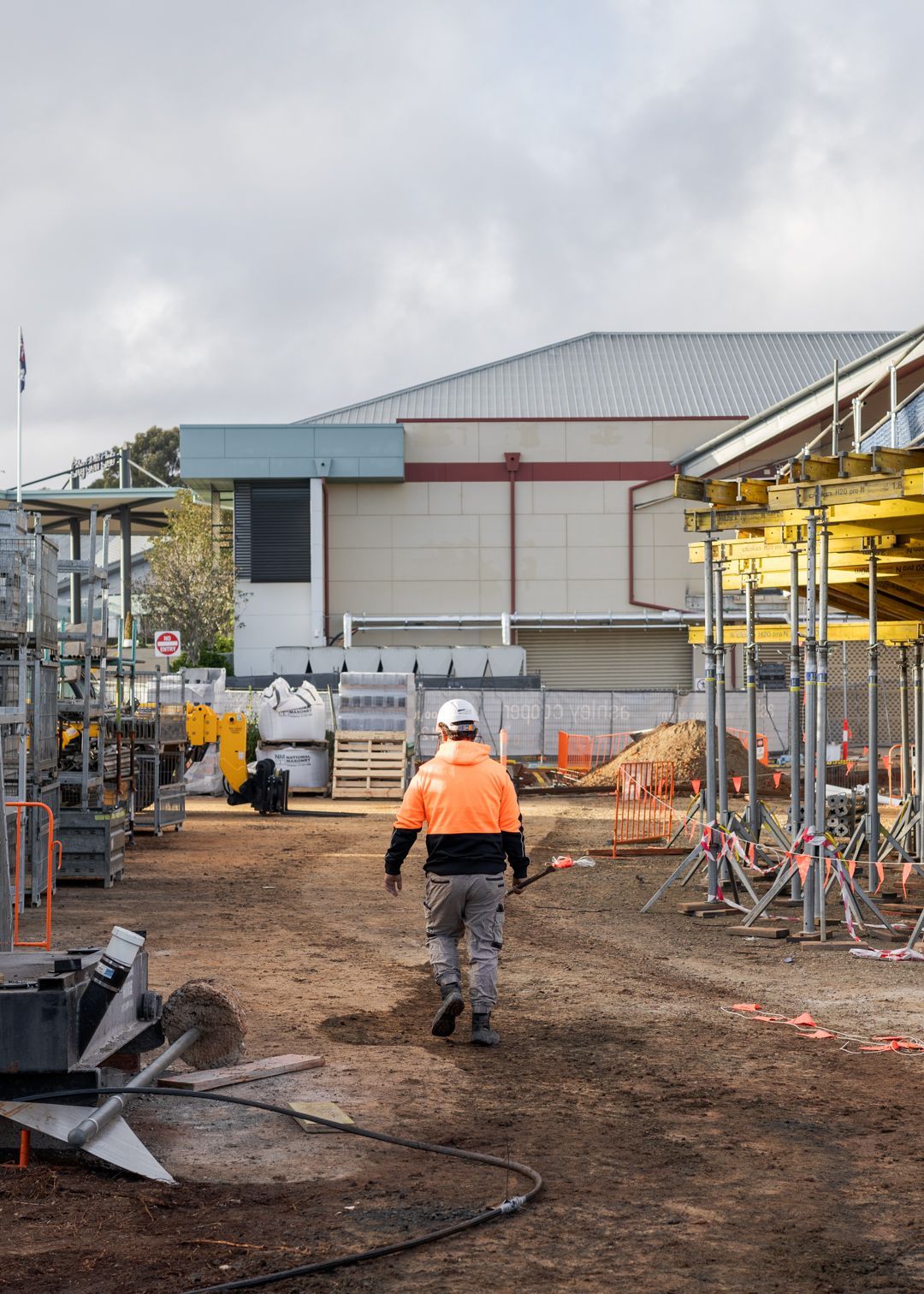 Worker in orange safety vest walking through an industrial construction site with scaffolding and machinery