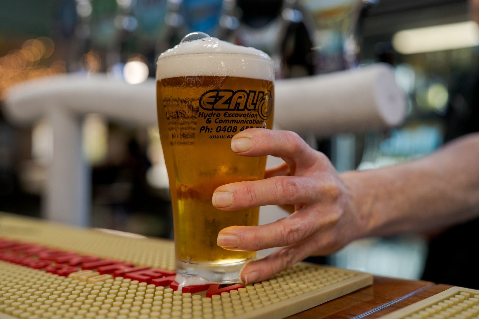 Hand holding a pint of beer on a bar counter, with a blurred restaurant background.