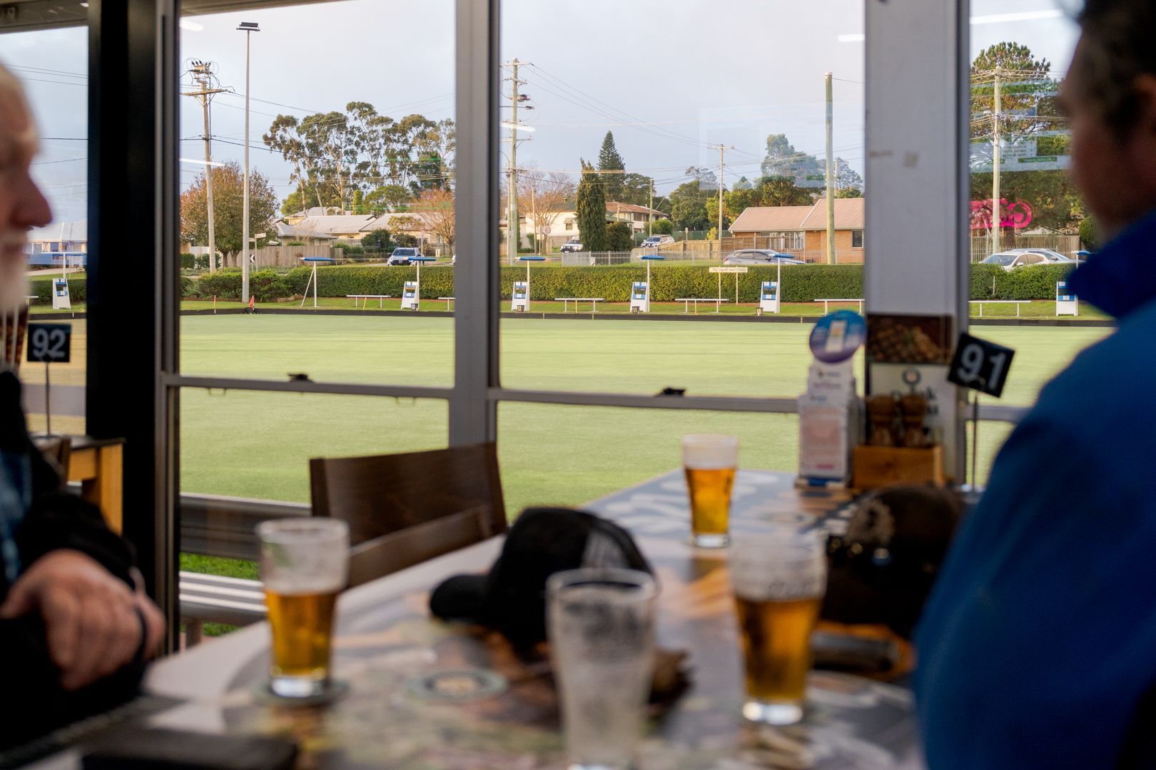People seated at a table in a café overlooking a green sports field through large windows.