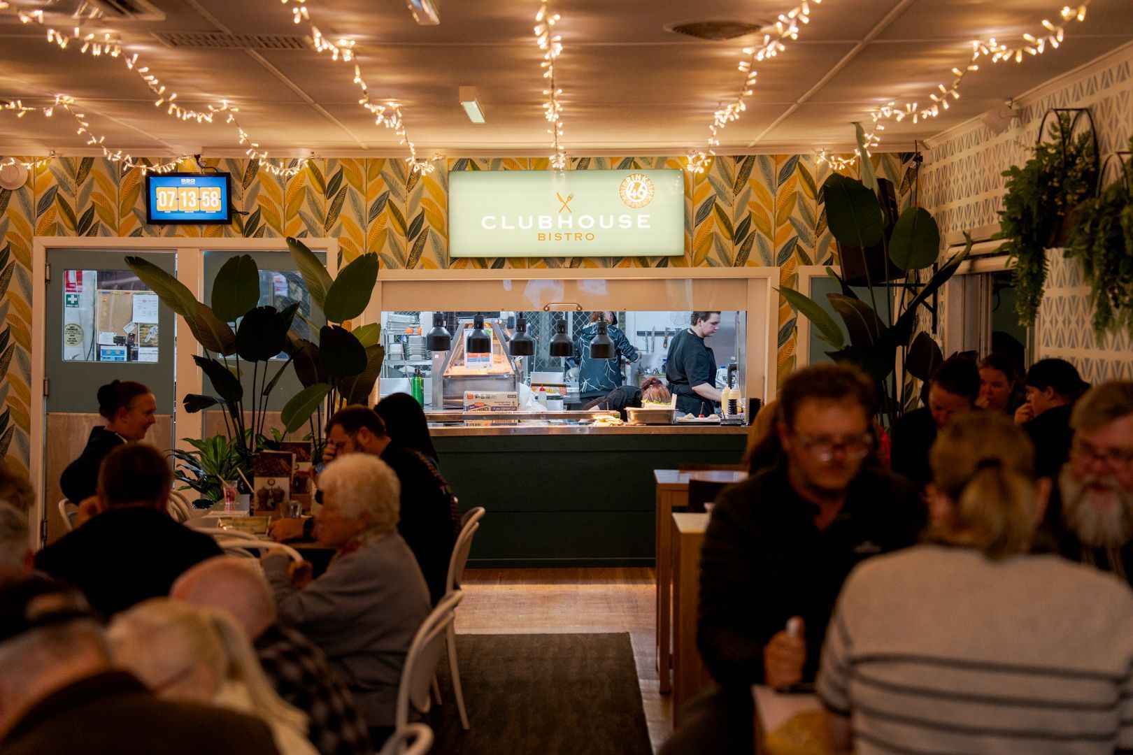 Cosy café interior with string lights, a counter in back, and patrons seated at tables.