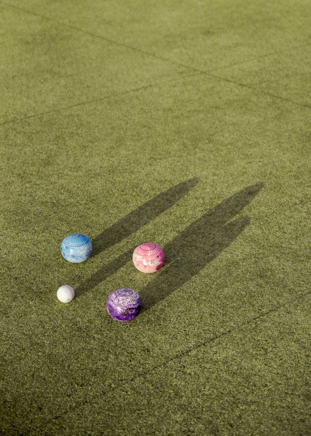 Three colored balls and a white ball on grass, with long shadows in sunlight