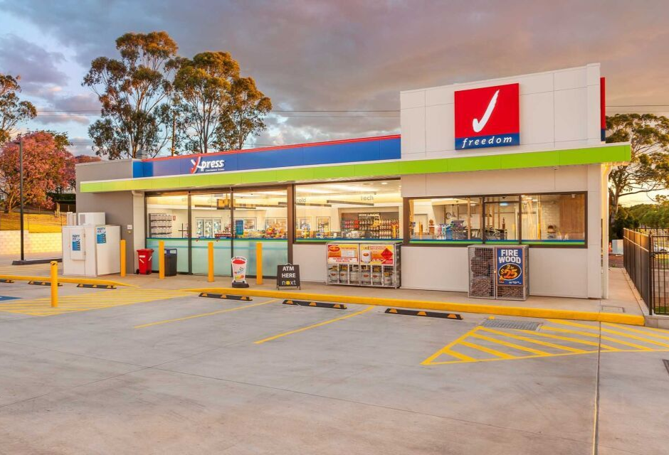 Exterior of a fuel station at dusk with lit storefront and parking area
