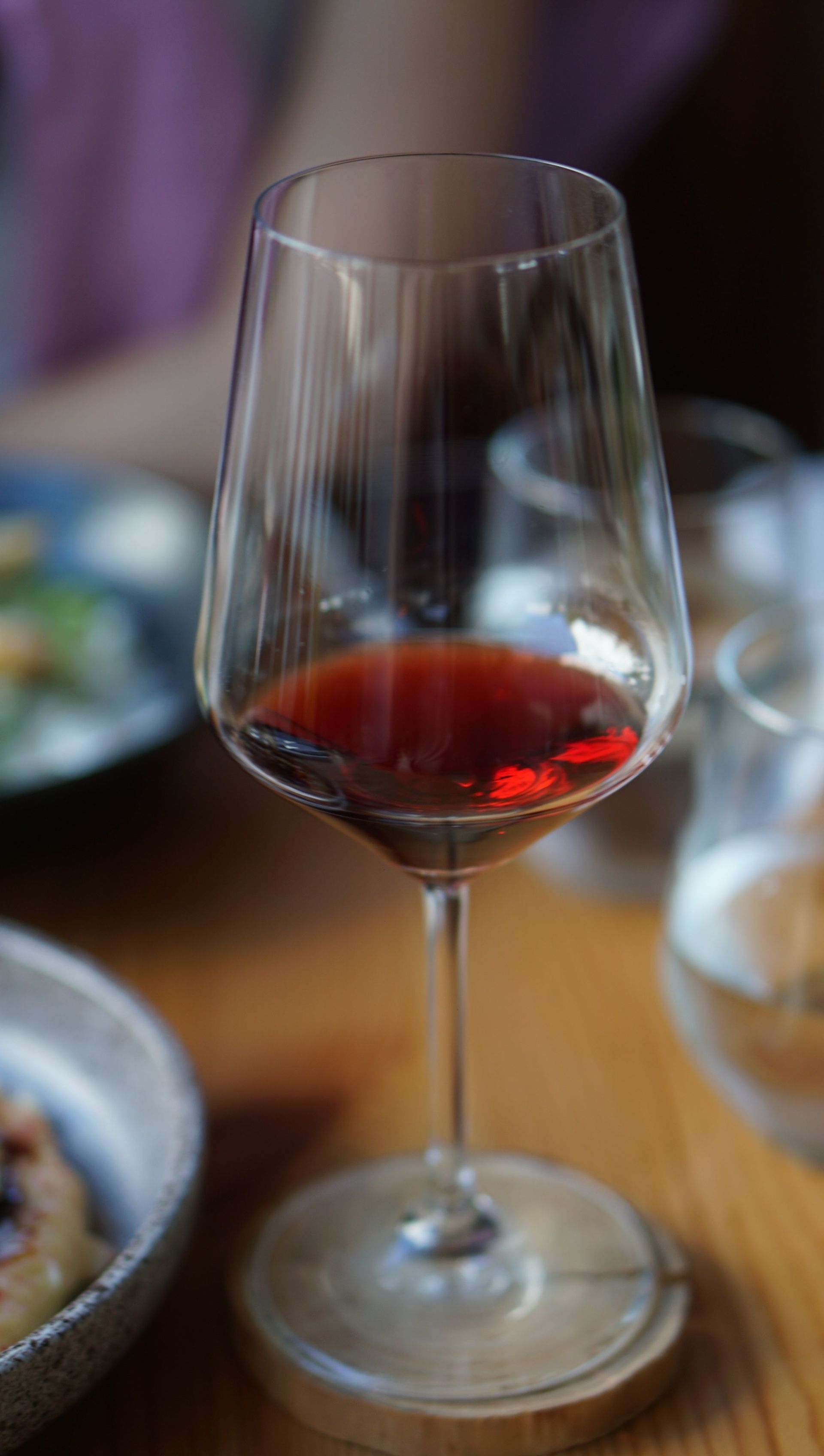 A wine glass with a small amount of red wine on a dining table.