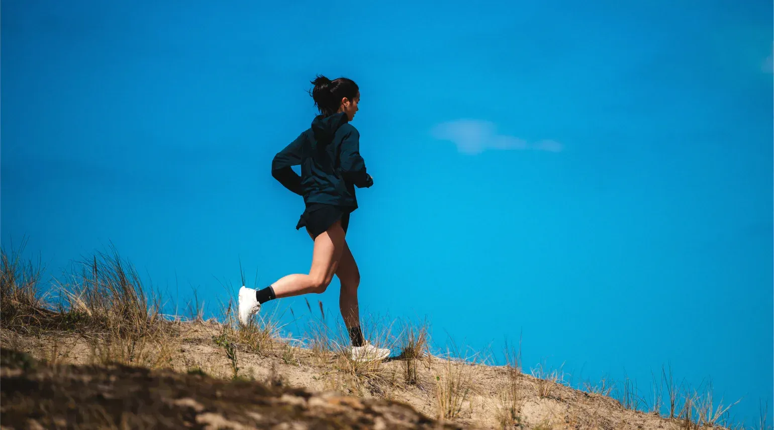Person running uphill on a sunny day with a bright blue sky.