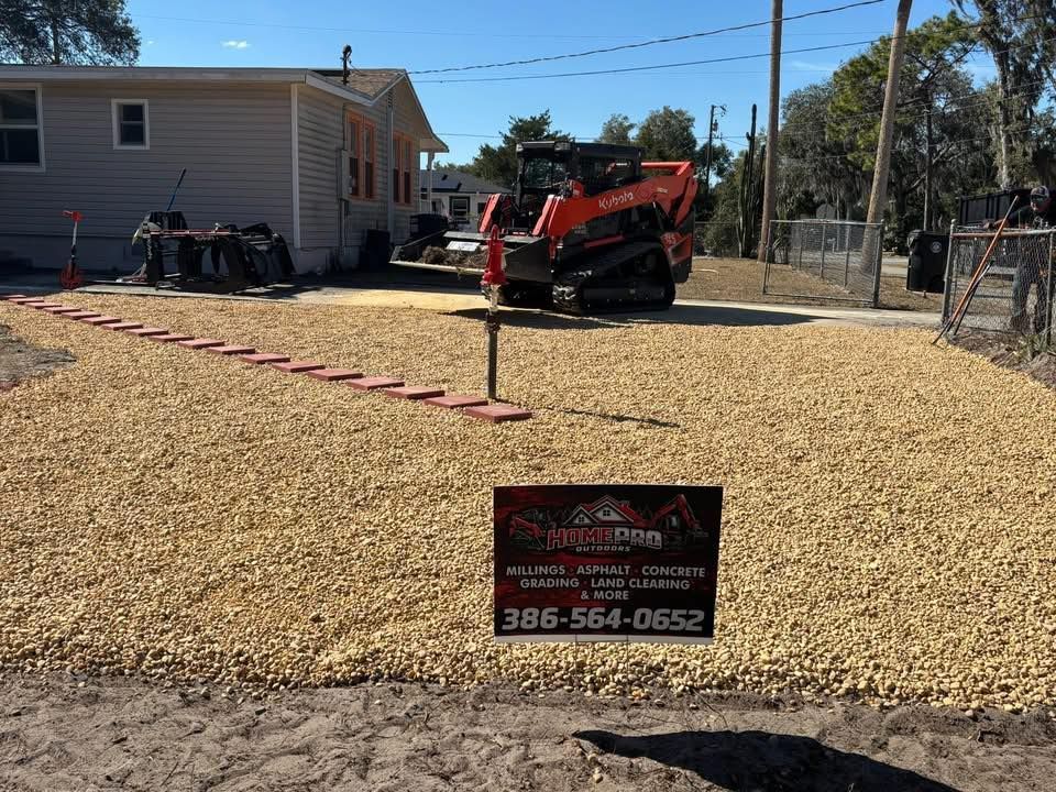 A construction site with a freshly spread gravel driveway and a skid-steer loader parked next to a house.