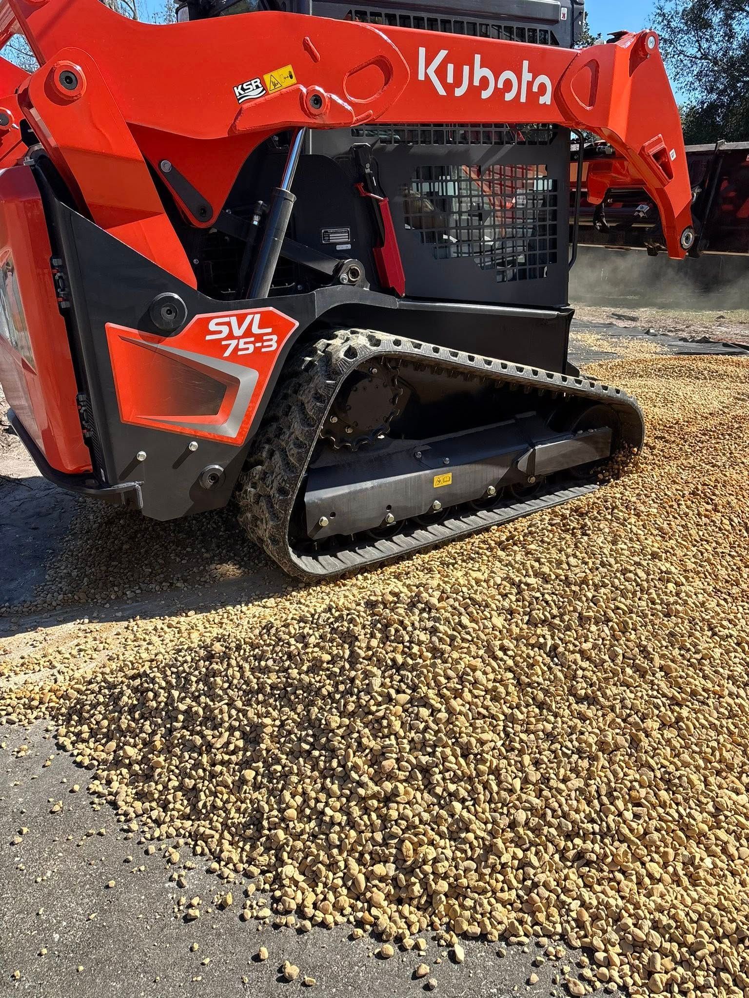 A bright orange Kubota SVL 75-3 track loader sits on a bed of gravel and dirt.