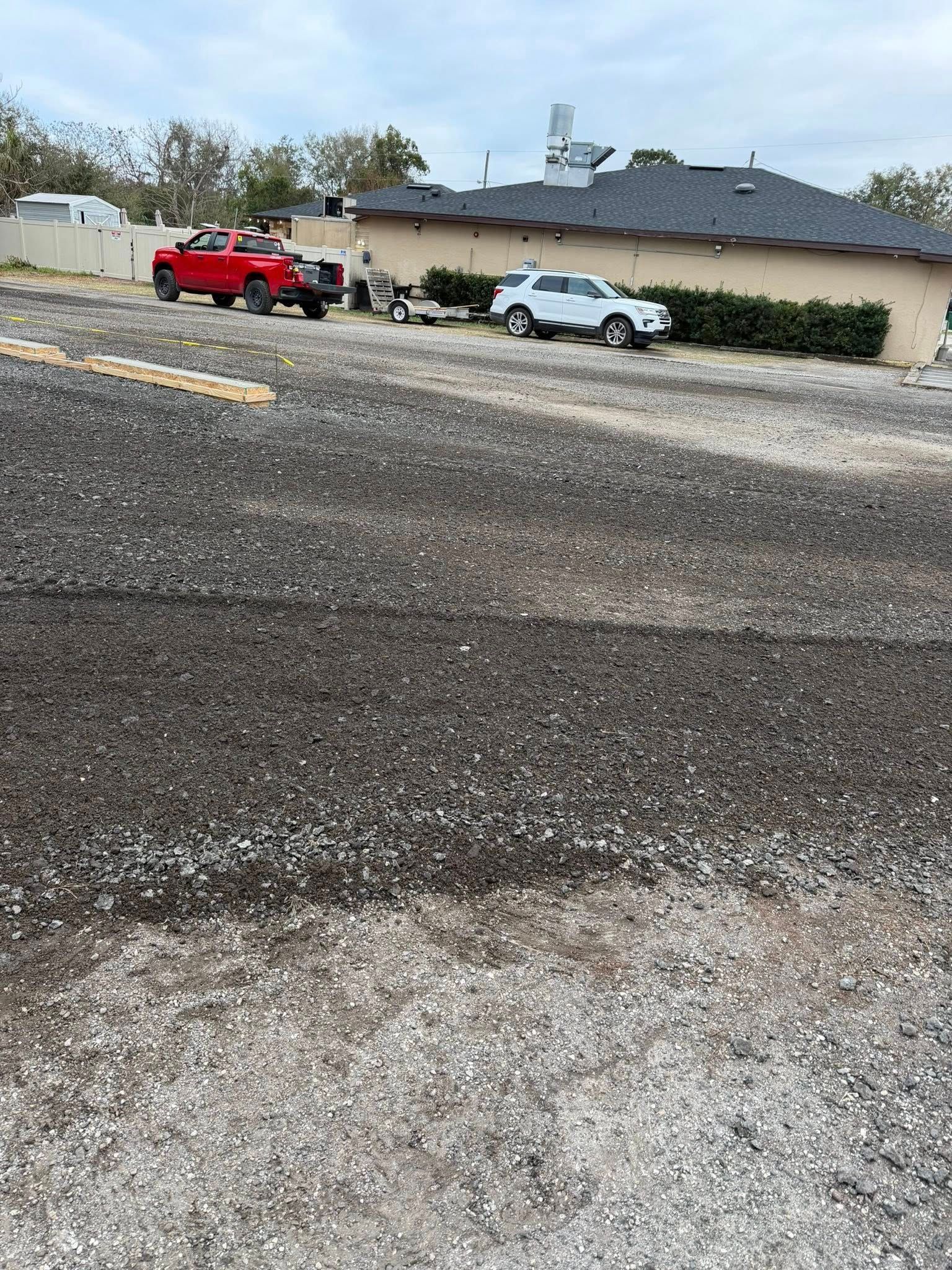 A red pickup truck towing a trailer and a white SUV parked on a gravel lot in front of a building with a dark roof.