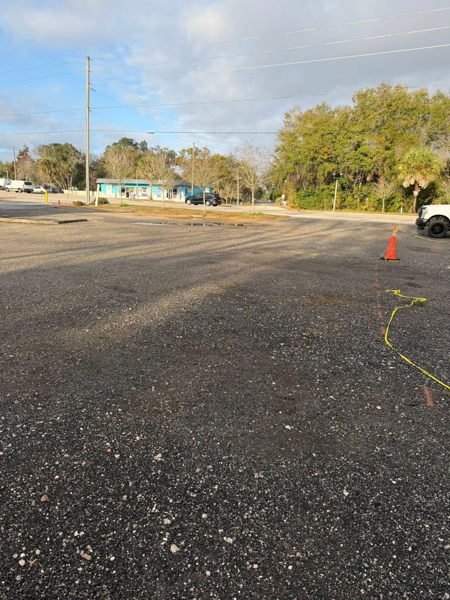 A gravel-covered parking lot on a sunny day with a teal building and trees in the distance.