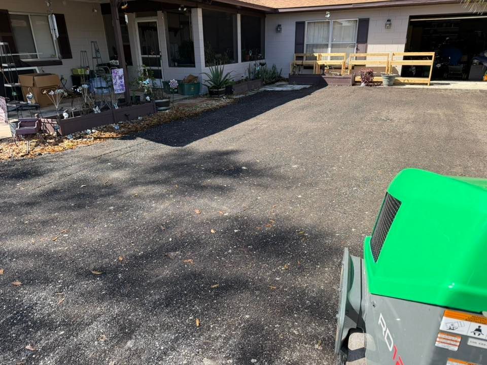 A view of a freshly laid asphalt driveway in front of a residential house with a green roller in the foreground.