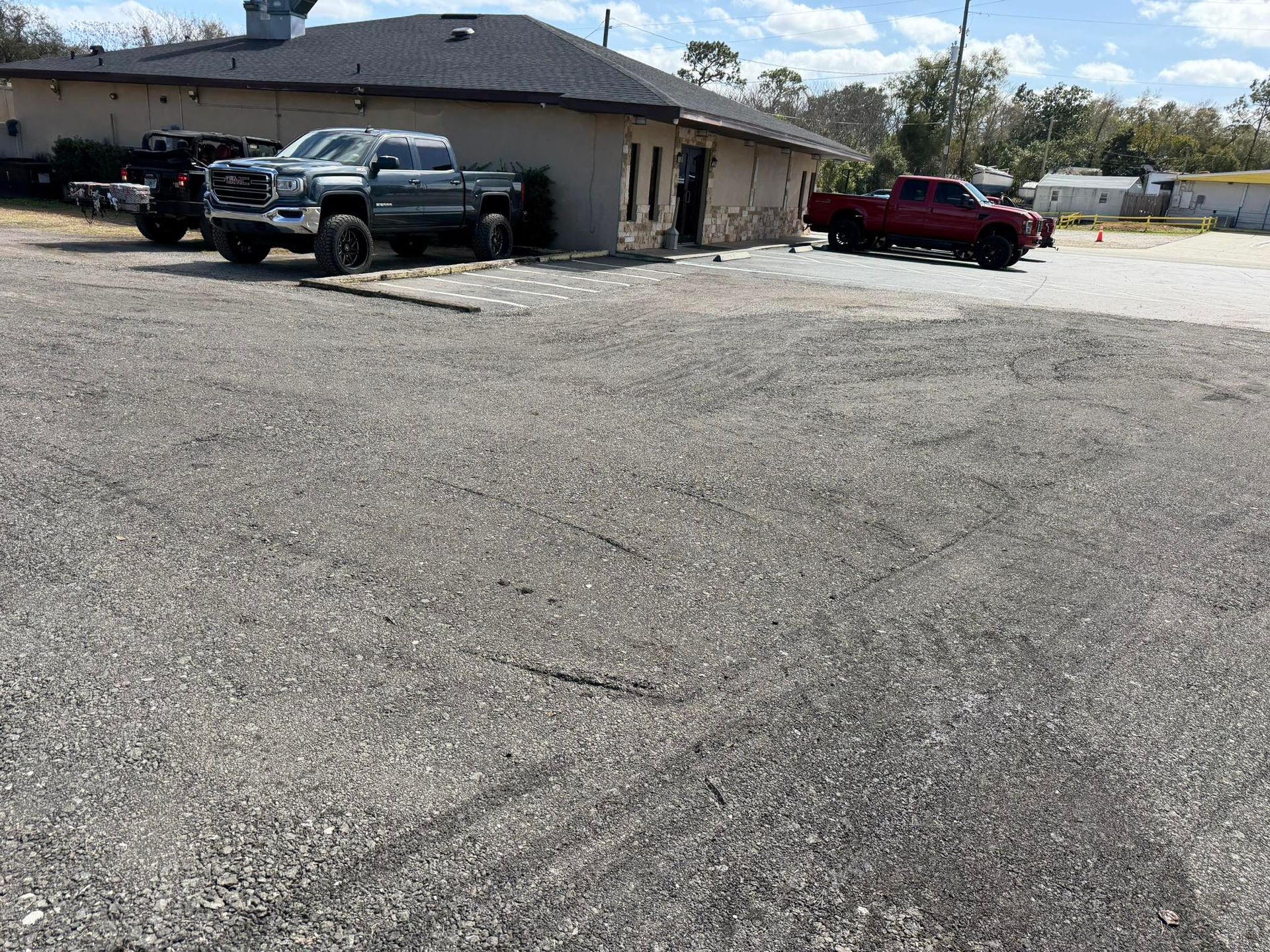 Two pickup trucks, one grey and one red, parked in front of a building with a gravel lot on a sunny day.