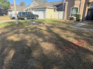 A residential lawn with red utility marking paint, a parked SUV, and a house in the background.