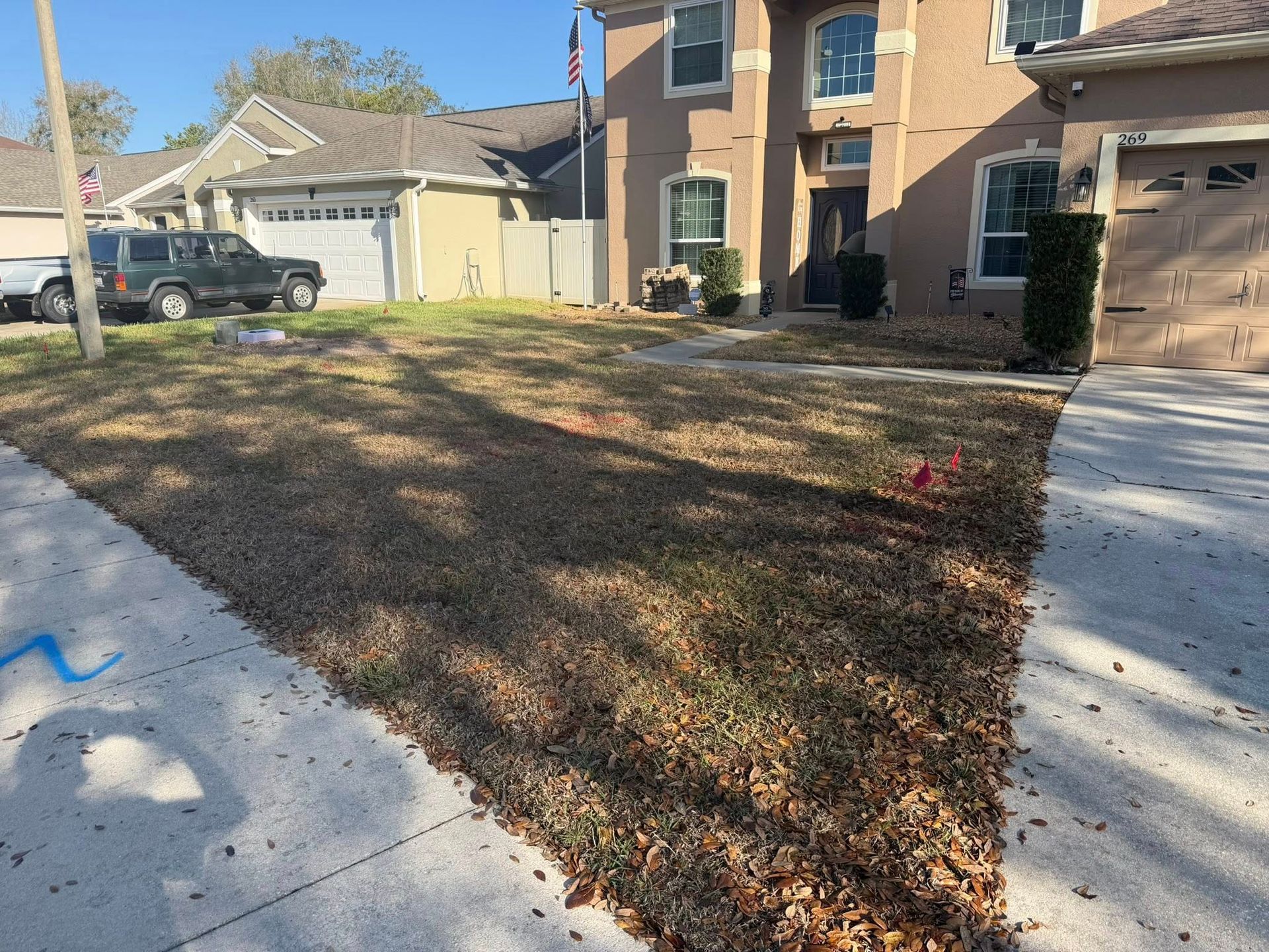 A suburban home with a dry, leaf-covered front lawn and a dark SUV parked in the driveway on a sunny day.