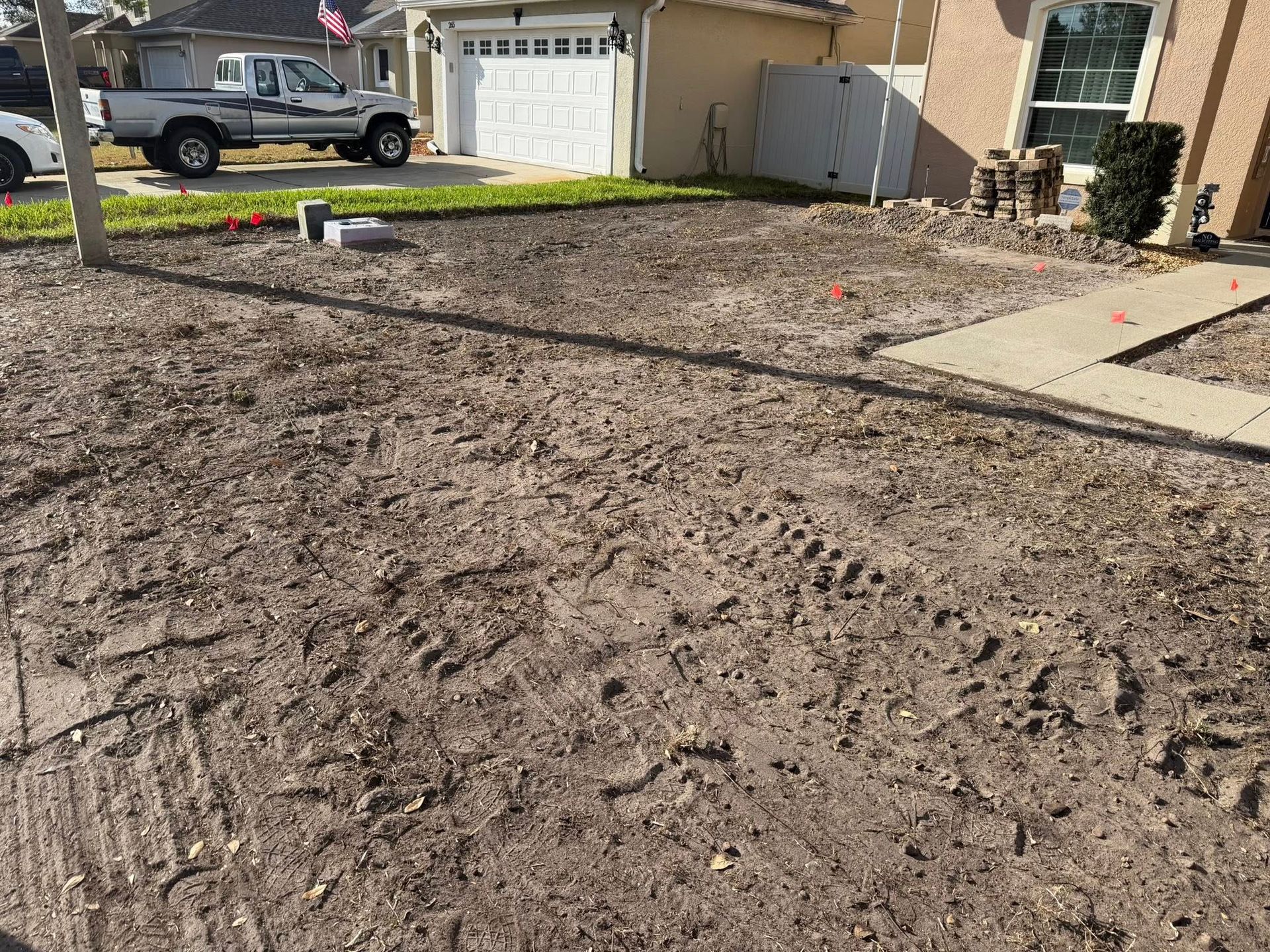 A residential front yard with exposed dirt and construction tracks, located in front of a house with a parked truck.