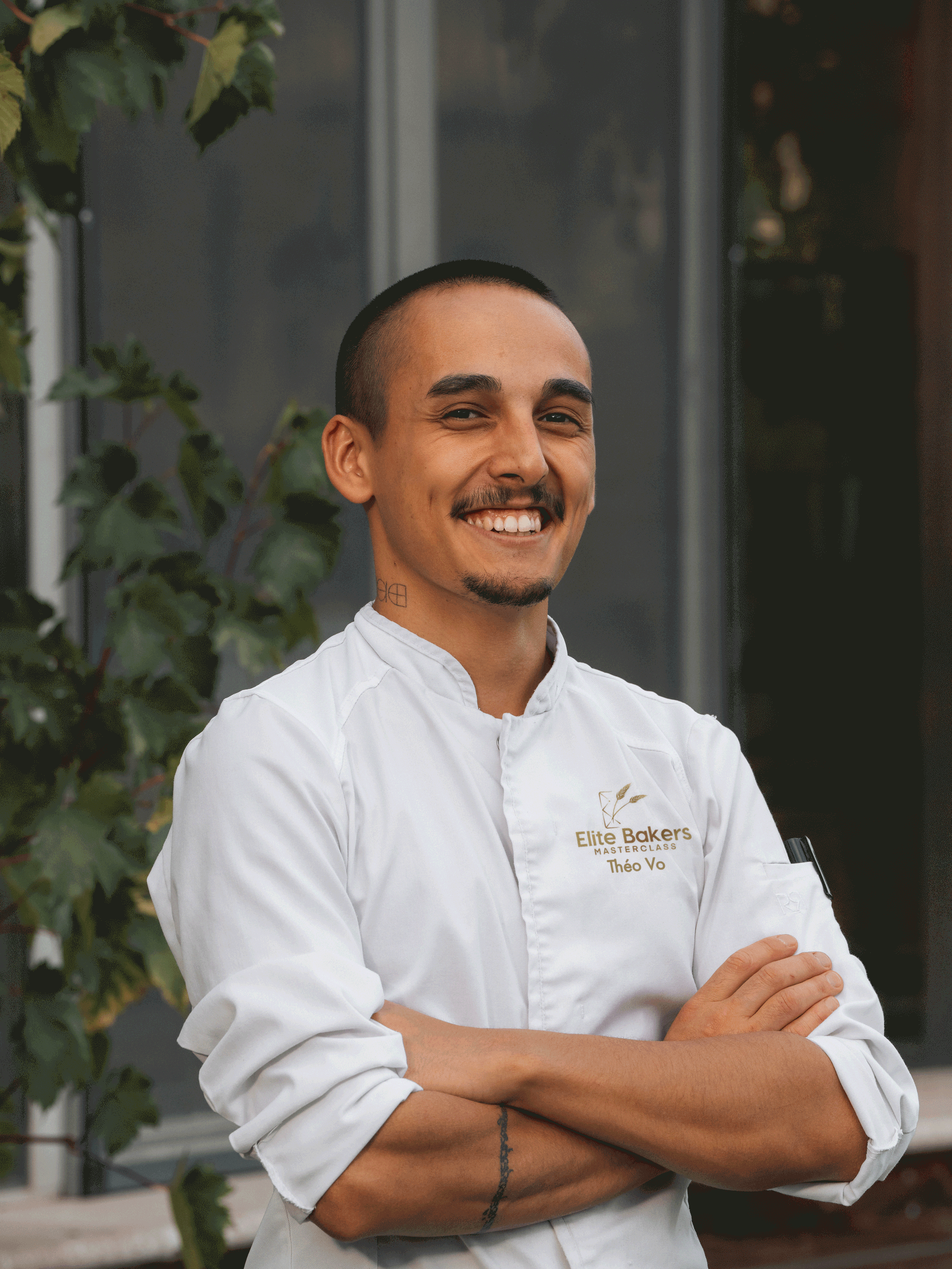 Un homme en veste blanche est debout, les bras croisés et souriant.