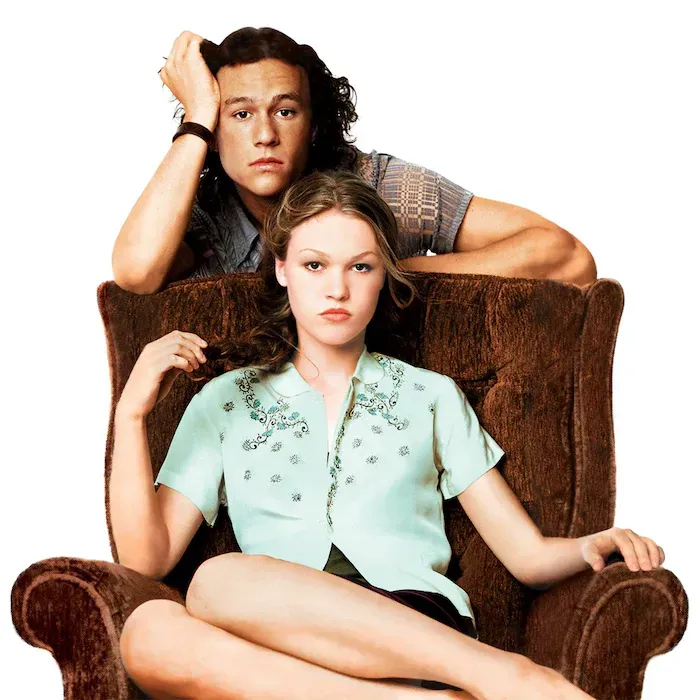 Heath Ledger leans on a couch behind Julia Stiles in a green blouse in Ten Things I Hate About You.