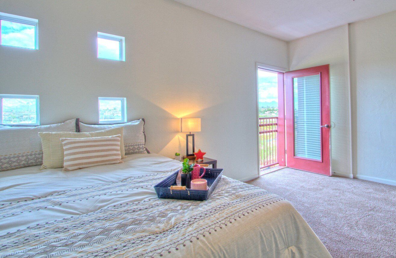 Floor plan options include private balconies, study nooks, and more! A fully furnished bedroom at The Seasons with private balcony, plush carpeting, and stylish decor with a bed tray.