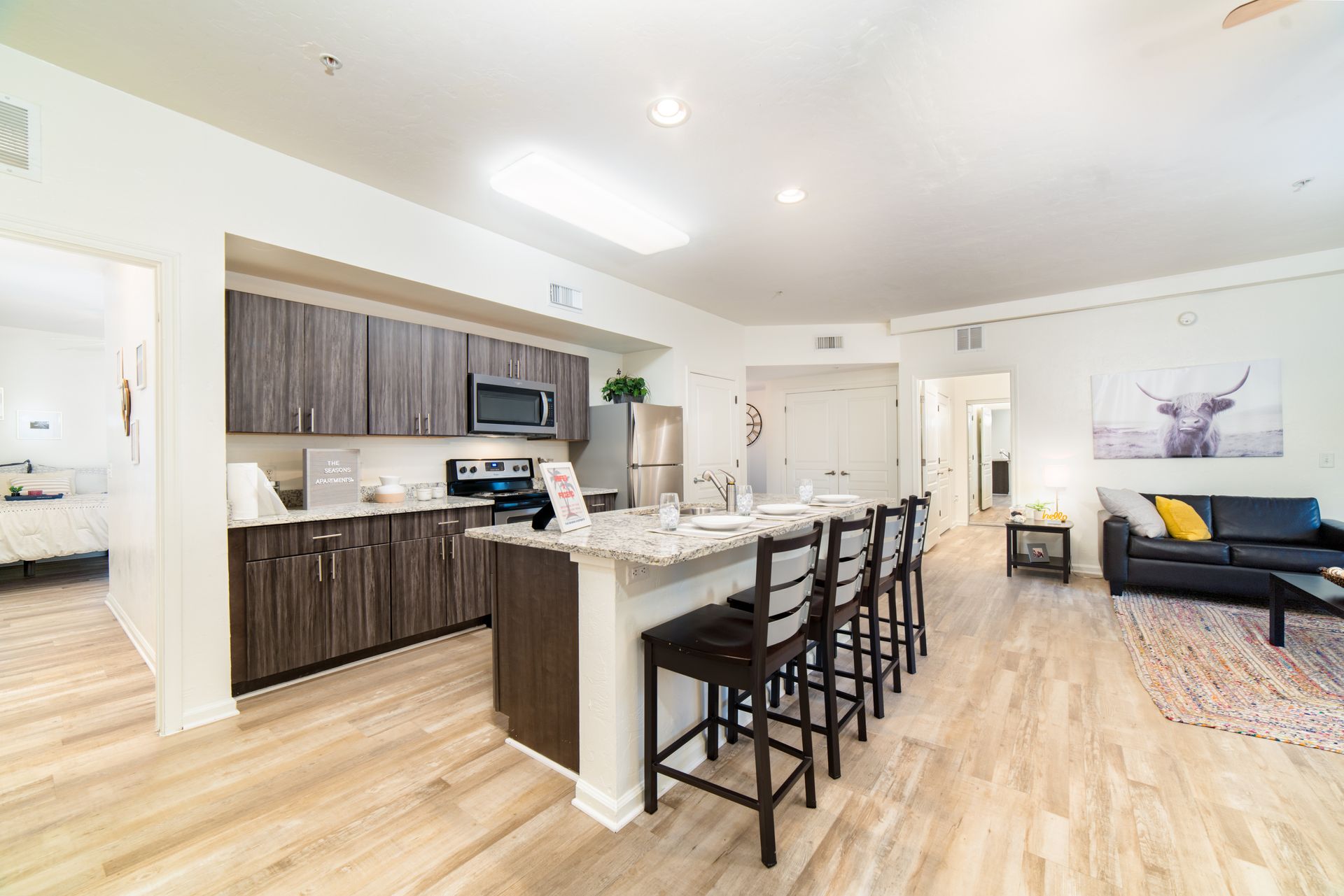 Invite friends and family over to cook and eat at your The Seasons Apartment! A four-seat island, fully furnished living room, and a peek into a private bedroom at The Seasons.