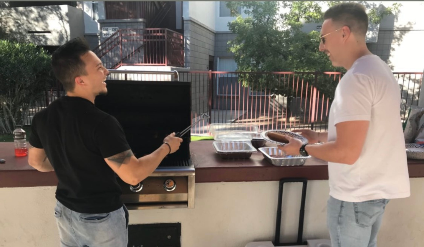 Male residents smiling while cooking and serving food using the BBQ grills by the pool.