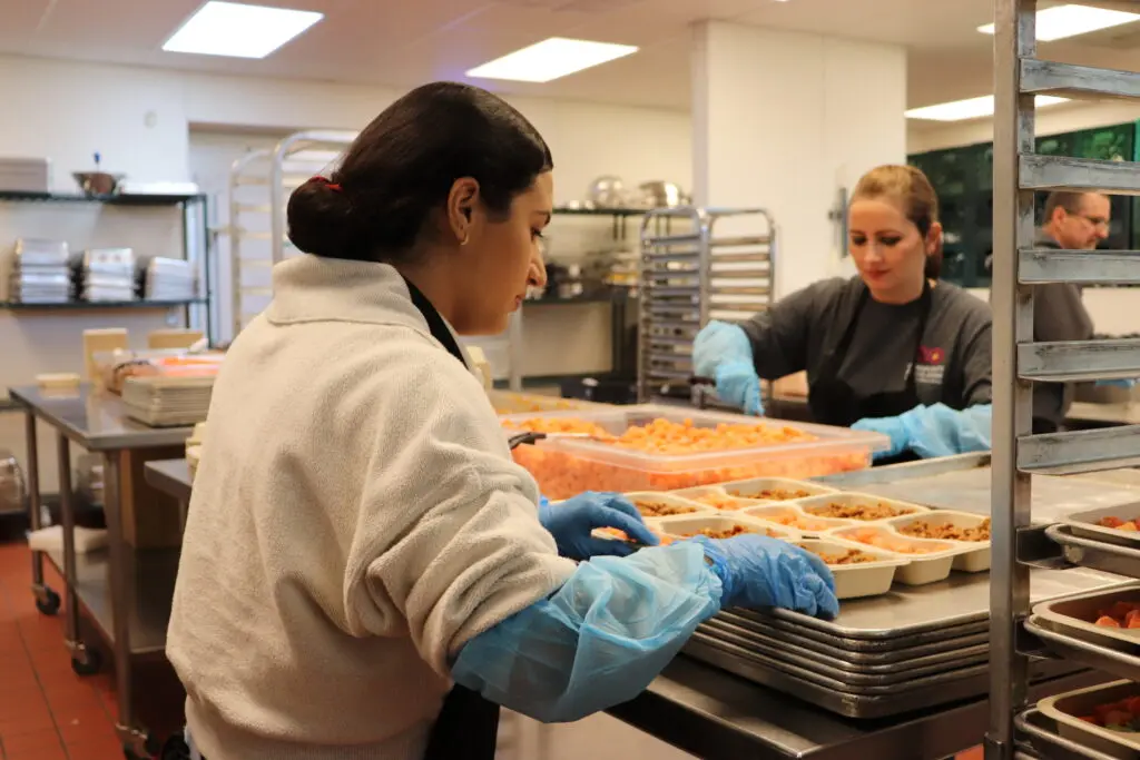 Give back to the community by volunteering! Three volunteers in hairnets and gloves prepare meals in Tucson at the Community Food Bank of Southern AZ.