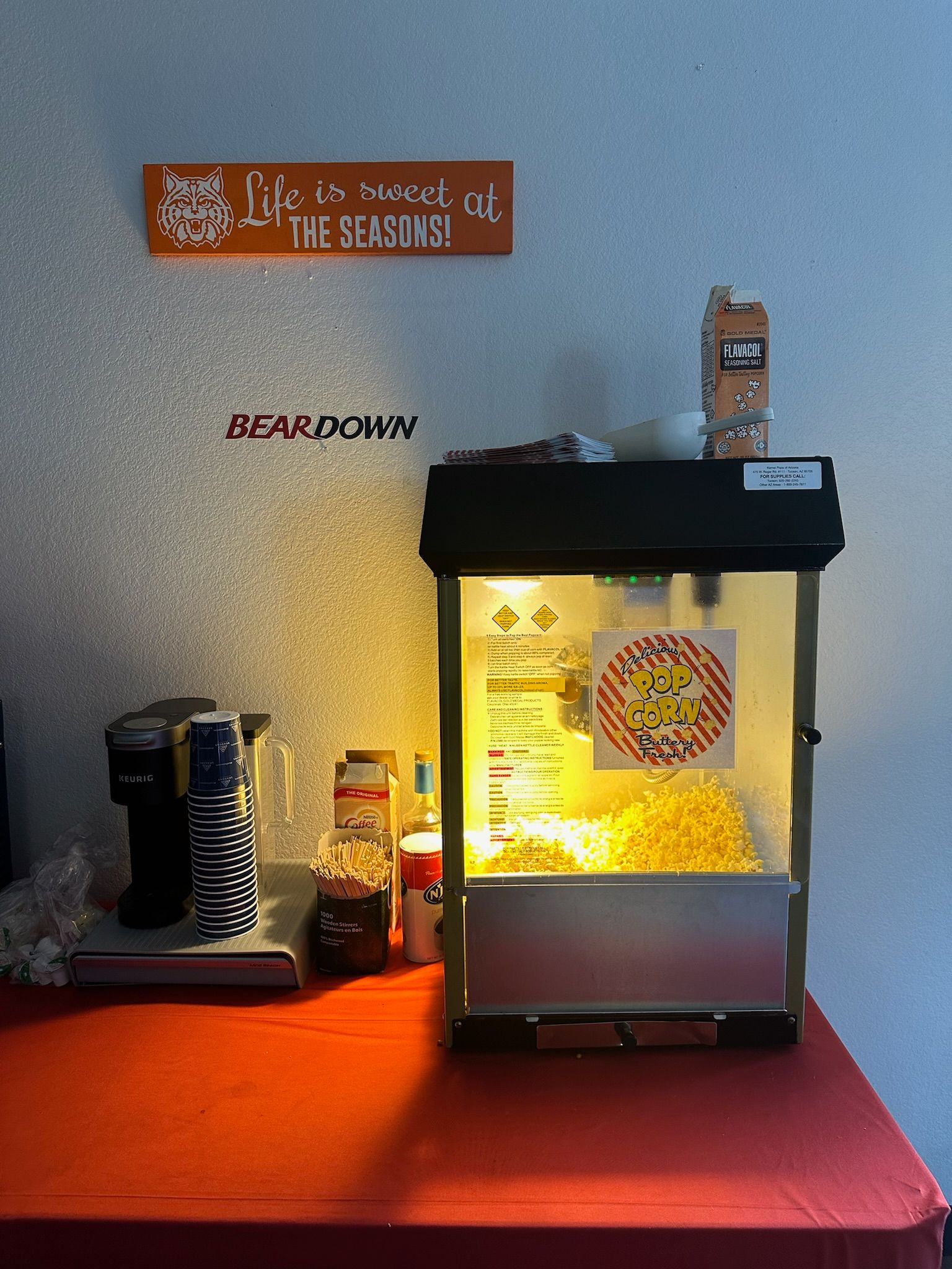 Fresh popcorn pops in a machine, with coffee cups and syrups nearby at the Clubhouse in The Seasons.