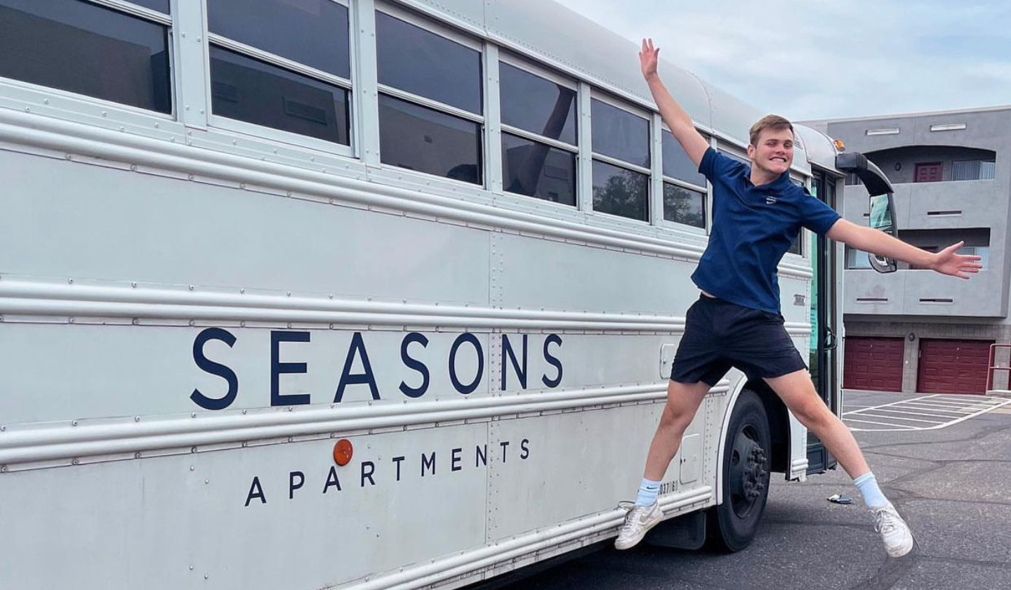 Male resident jumping excitedly next to the Seasons Apartments free shuttle to the university.