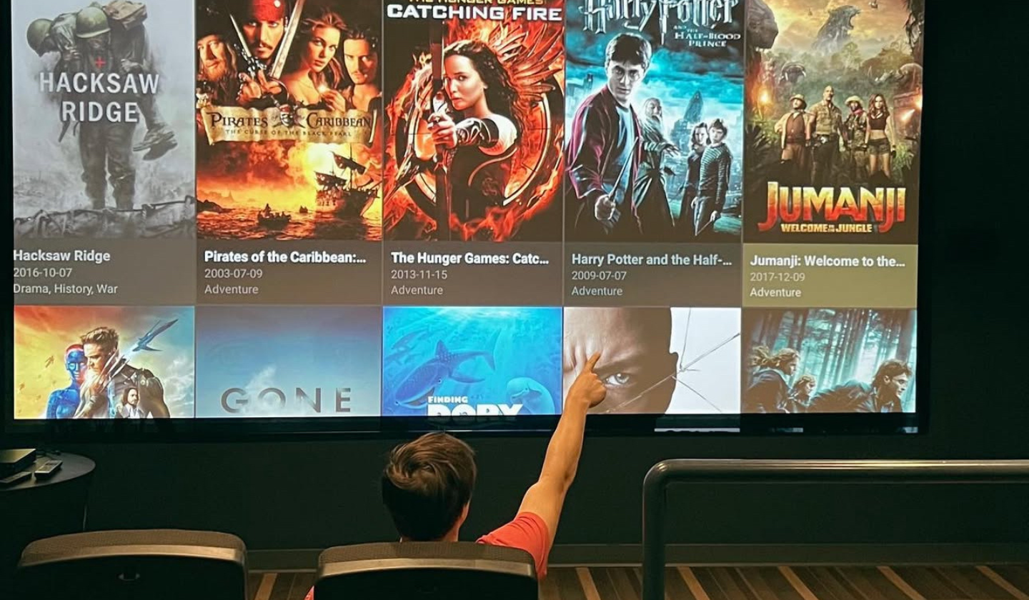 Connect from any device with an HDMI chord! Male resident picking which movie to stream at The Seasons' on-site movie theater with lounge chairs and a big screen.