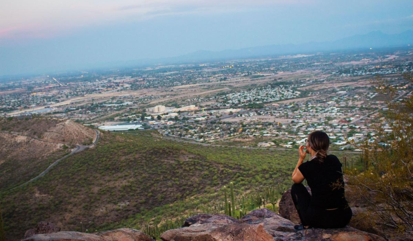 Make sure to pack a lot of water for your hike! A female hiker sitting and taking in the view at the top of the Tumamoc trail.