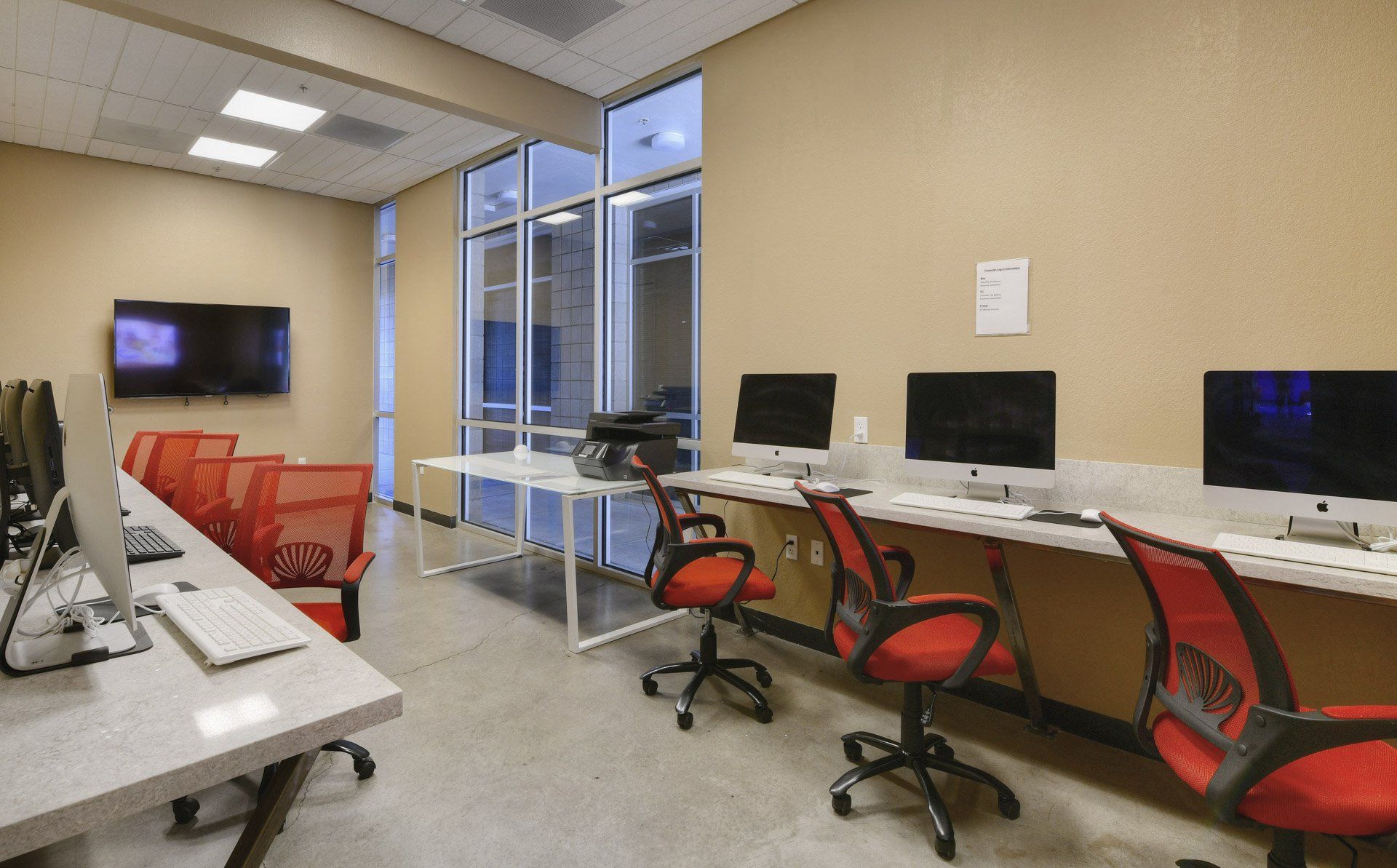 Use the computer lab at The Seasons to study! A view of The Seasons' Computer lab with iMacs, Dells, and red office chairs.