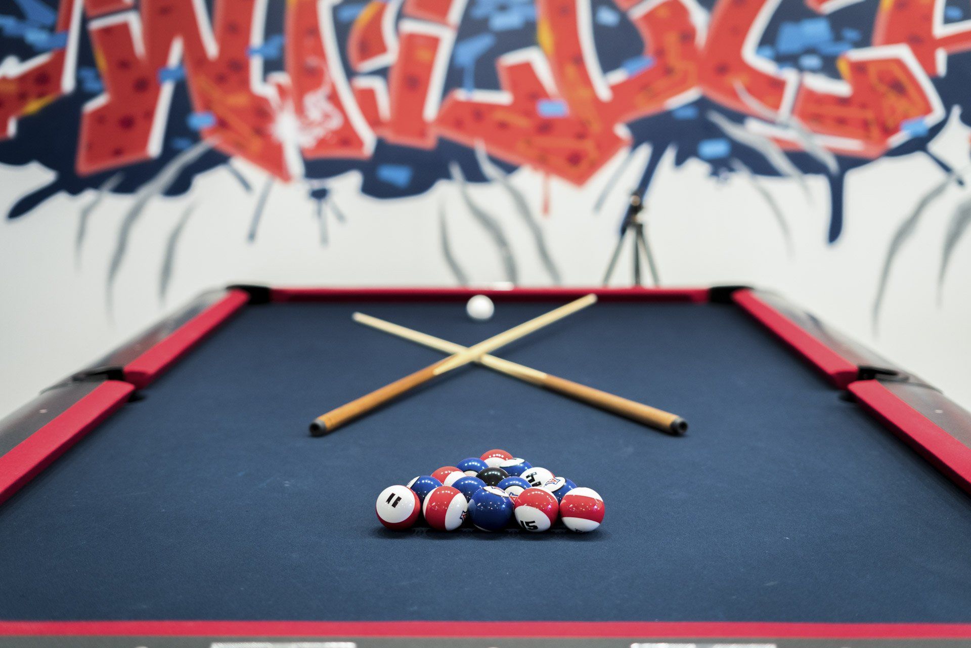 Hang with your friends at the Clubhouse! A red and navy pool table with a triangle of pool balls and cue sticks at The Seasons Clubhouse.