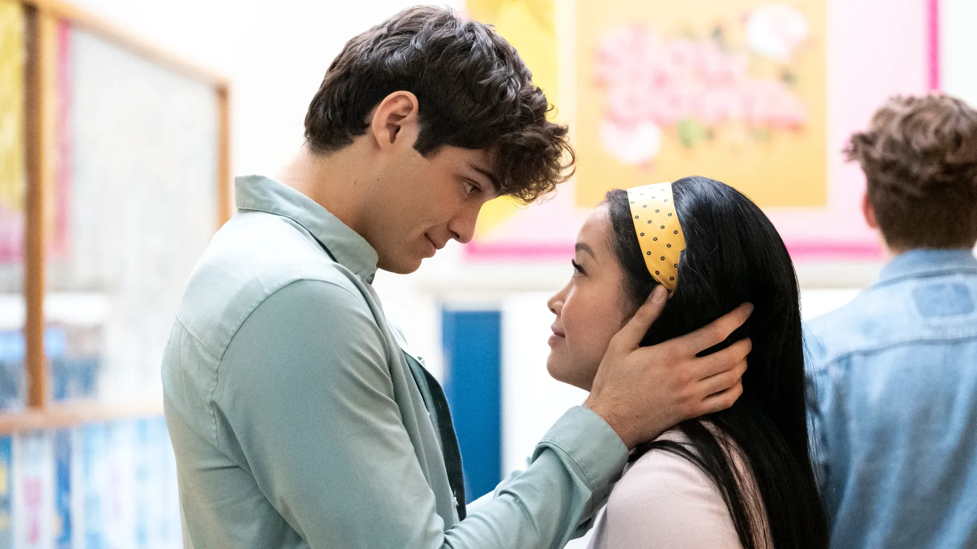 Peter Kavinsky and Lara Jean smile at each other in a high school hallway in To All the Boys I've Loved Before.