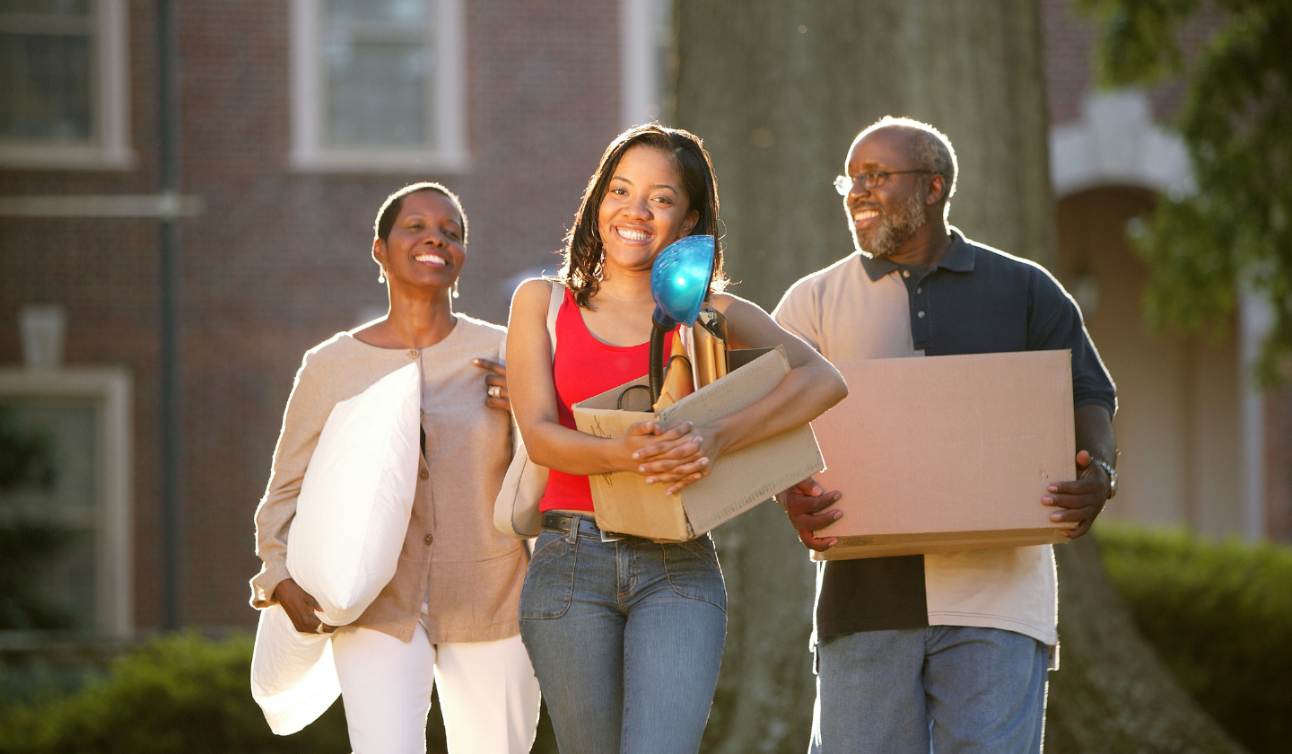 Help your student(s) move into The Seasons! Mom is smiling holding a pillow, dad is smiling holding a moving box, freshman daughter is smiling holding a moving box