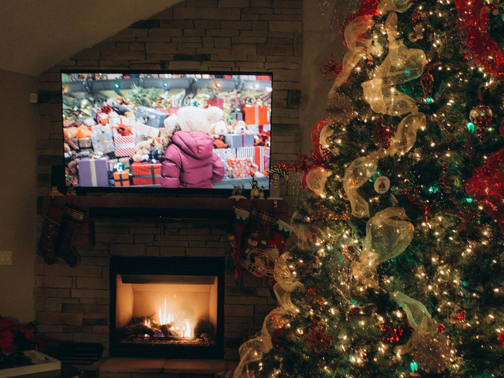 Decorate your apartment to really get in the festive spirit! A living room decorated for Christmas with a Christmas tree, fire place, and a holiday movie playing on the big screen TV.