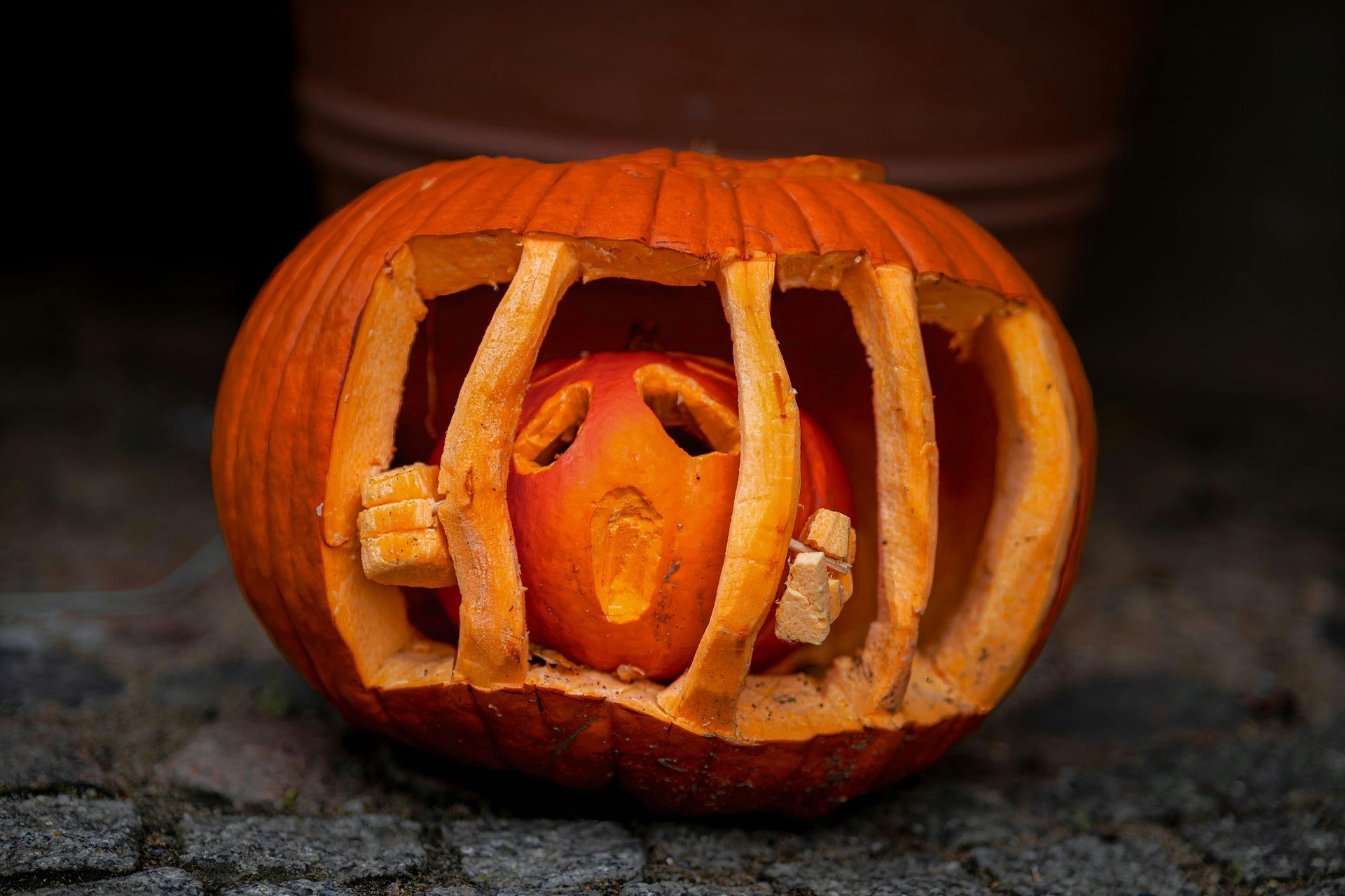 A carved pumpkin that looks like a little pumpkin is jailed inside of a bigger pumpkin.
