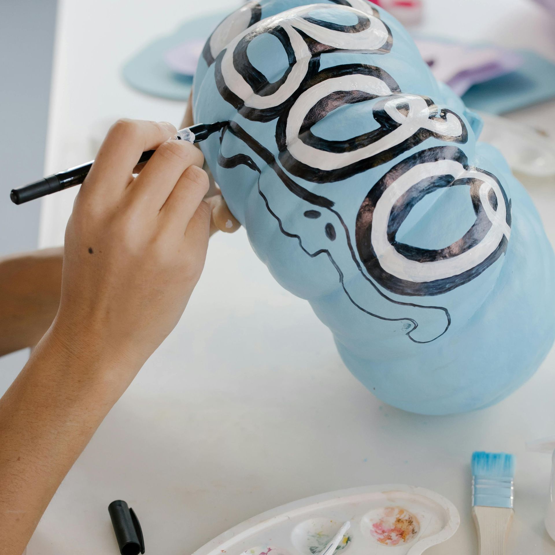 Try painting pumpkins instead of carving! A hand outlines a ghost on a blue pumpkin that reads